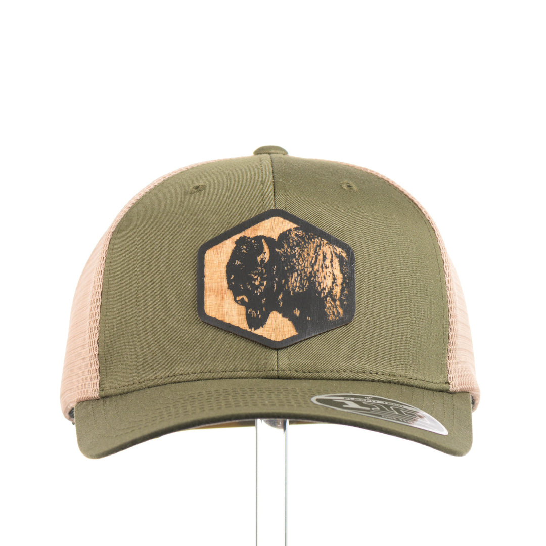 The front of an olive green and khaki mesh flexfit trucker hat with a bison flexwood hexagon patch.