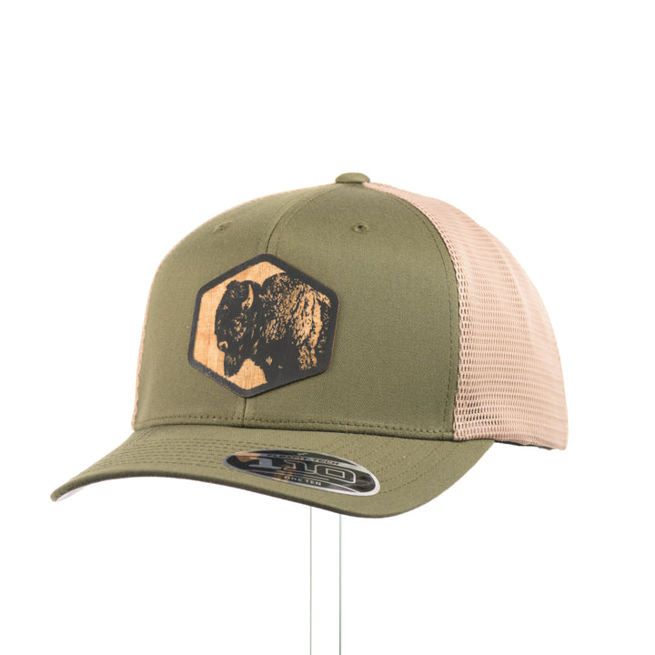 An olive green and khaki mesh flexfit trucker hat with a bison flexwood hexagon patch at a quarter turn.