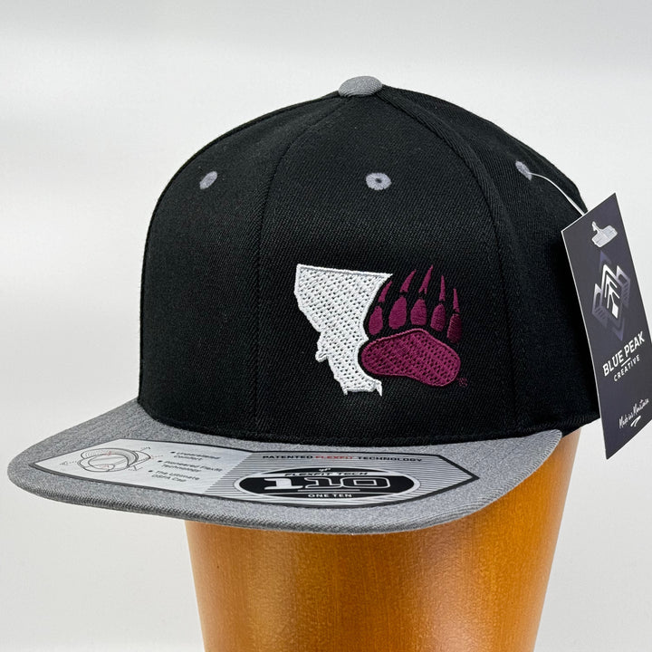 Black Montana Paw - Wool Flat Bill Hat made in Missoula, MT (home of the UM Grizzlies) by Blue Peak Creative—a black flat bill hat embroidered with a bear paw and the western edge of the state of Montana (3/4 view).