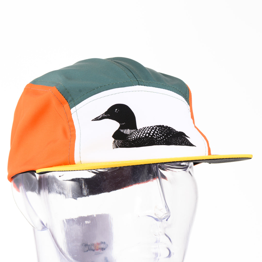 Loon Technical Camp Hat, an adjustable unstructured orange, teal, and white cap with a yellow bill, featuring a black and white drawing of a loon by Montana artist Brittany Finch; made in USA