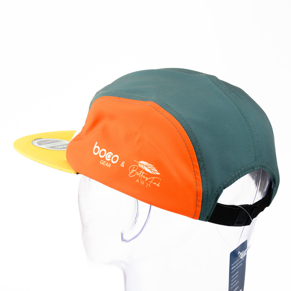 Loon Technical Camp Hat, an adjustable unstructured orange, teal, and white cap with a yellow bill, featuring a black and white drawing of a loon by Montana artist Brittany Finch; made in USA