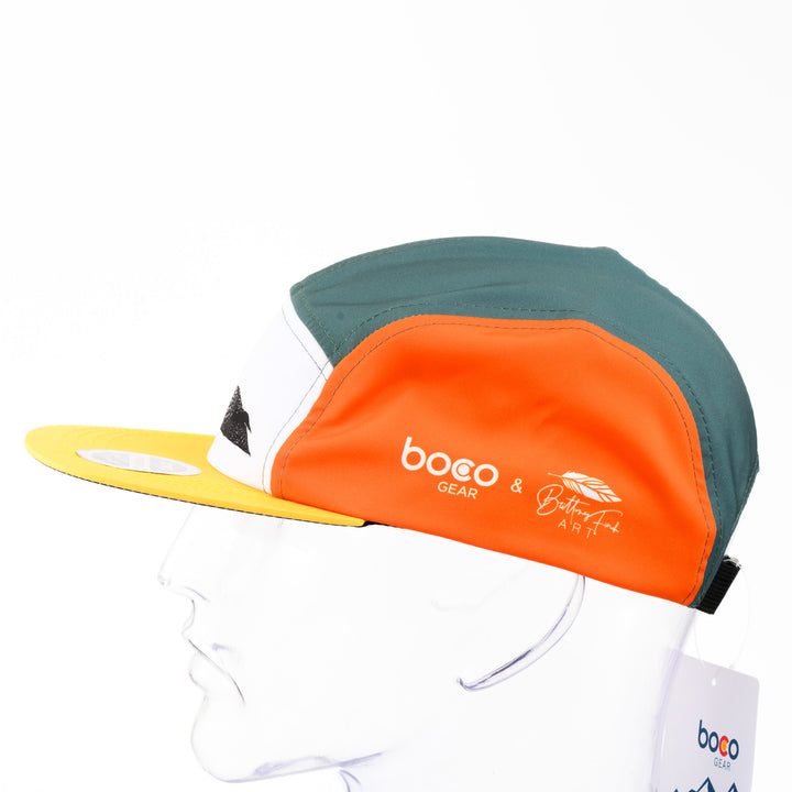 Loon Technical Camp Hat, an adjustable unstructured orange, teal, and white cap with a yellow bill, featuring a black and white drawing of a loon by Montana artist Brittany Finch; made in USA