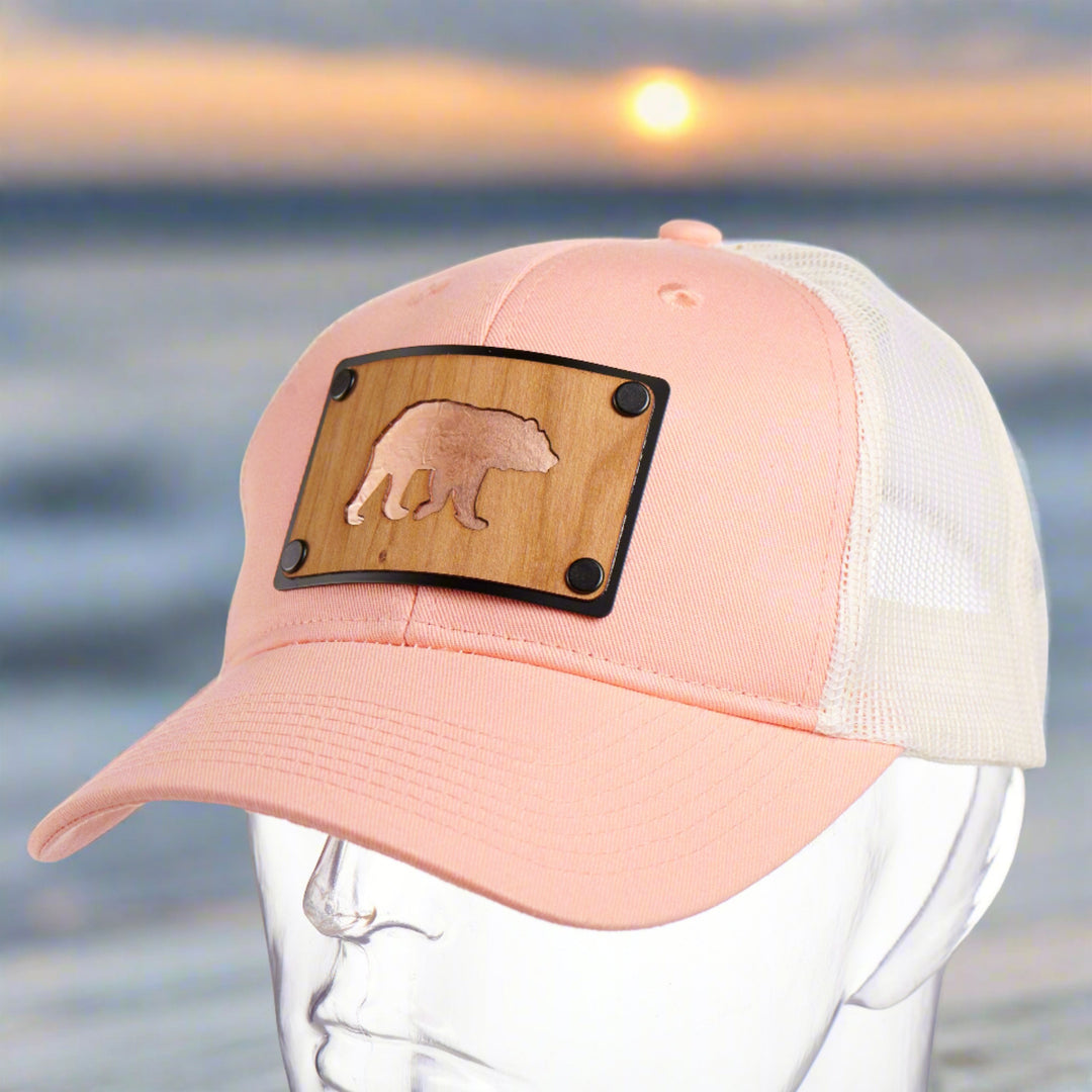 A peach trucker hat with a cherry wood and copper bear patch