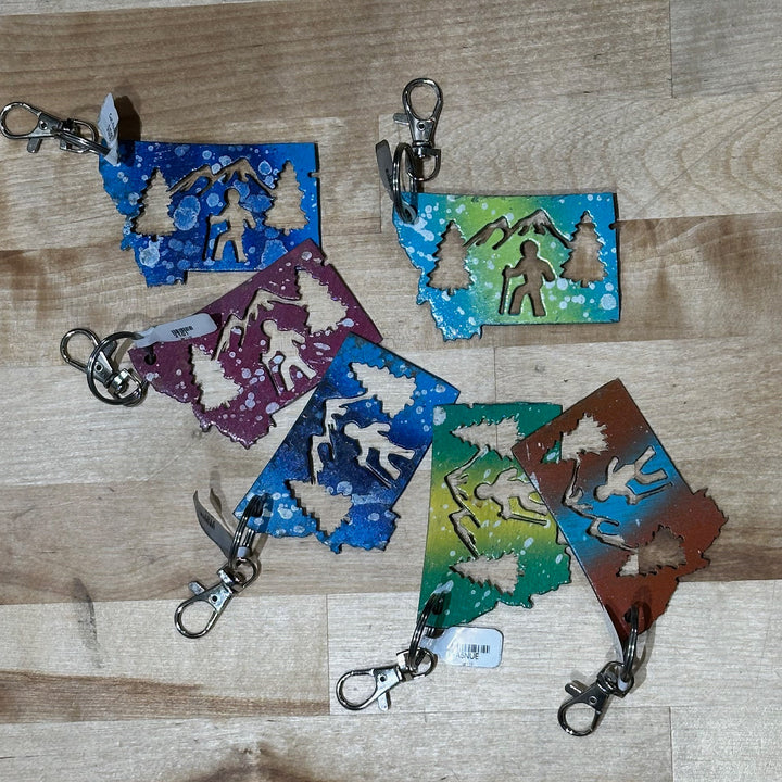 This made in Montana Hiker Metal Keychain showcases a state-shaped design with a hiker, mountains and trees cut out of it.