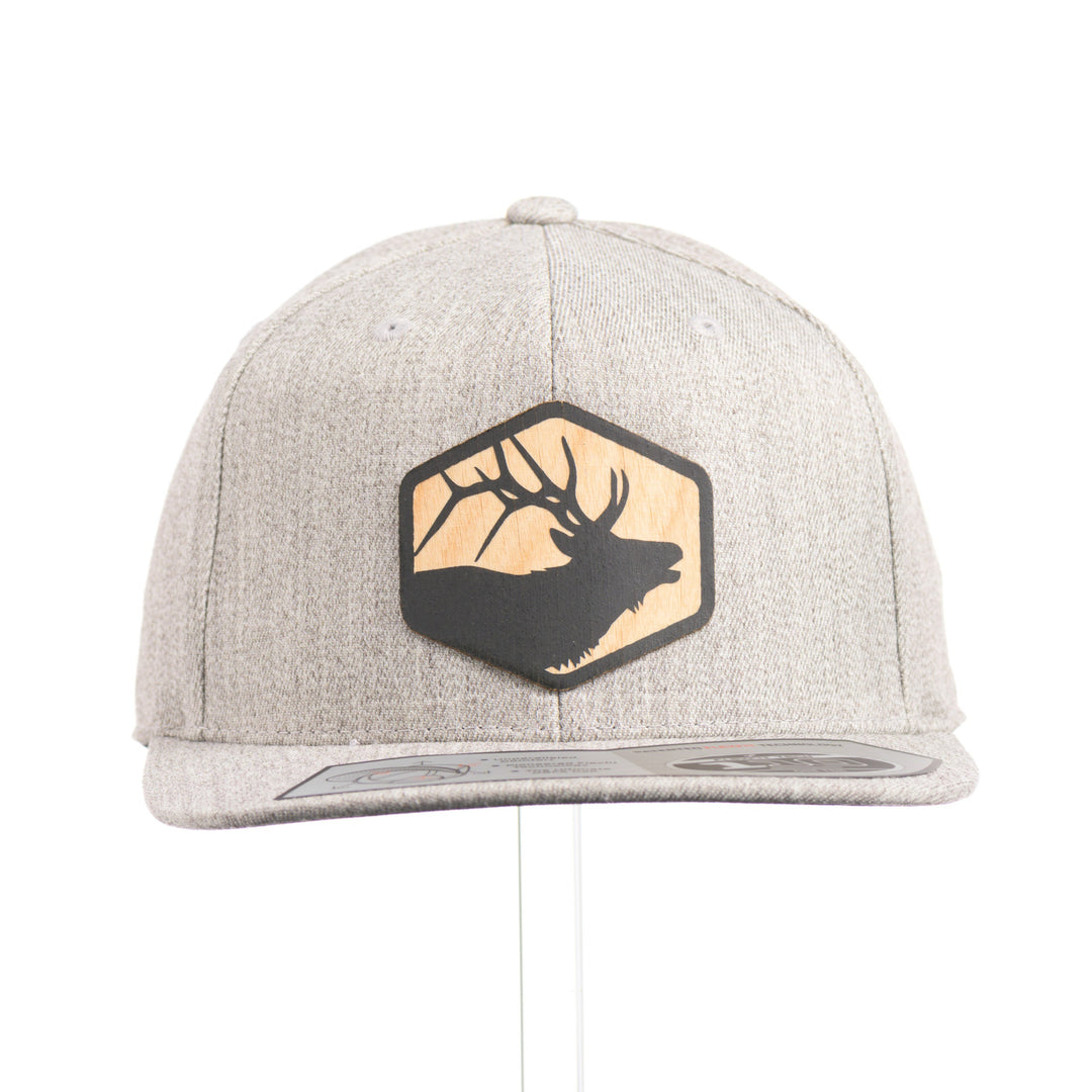 The front of a heather grey flexfit flat bill hat with a hexagon elk silhouette flexwood patch.