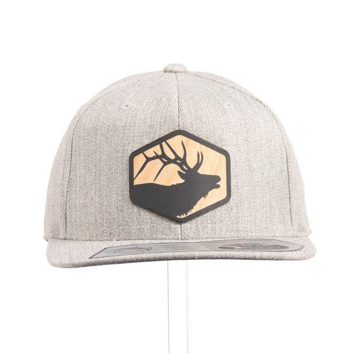 The front of a heather grey flexfit flat bill hat with a hexagon elk silhouette flexwood patch.
