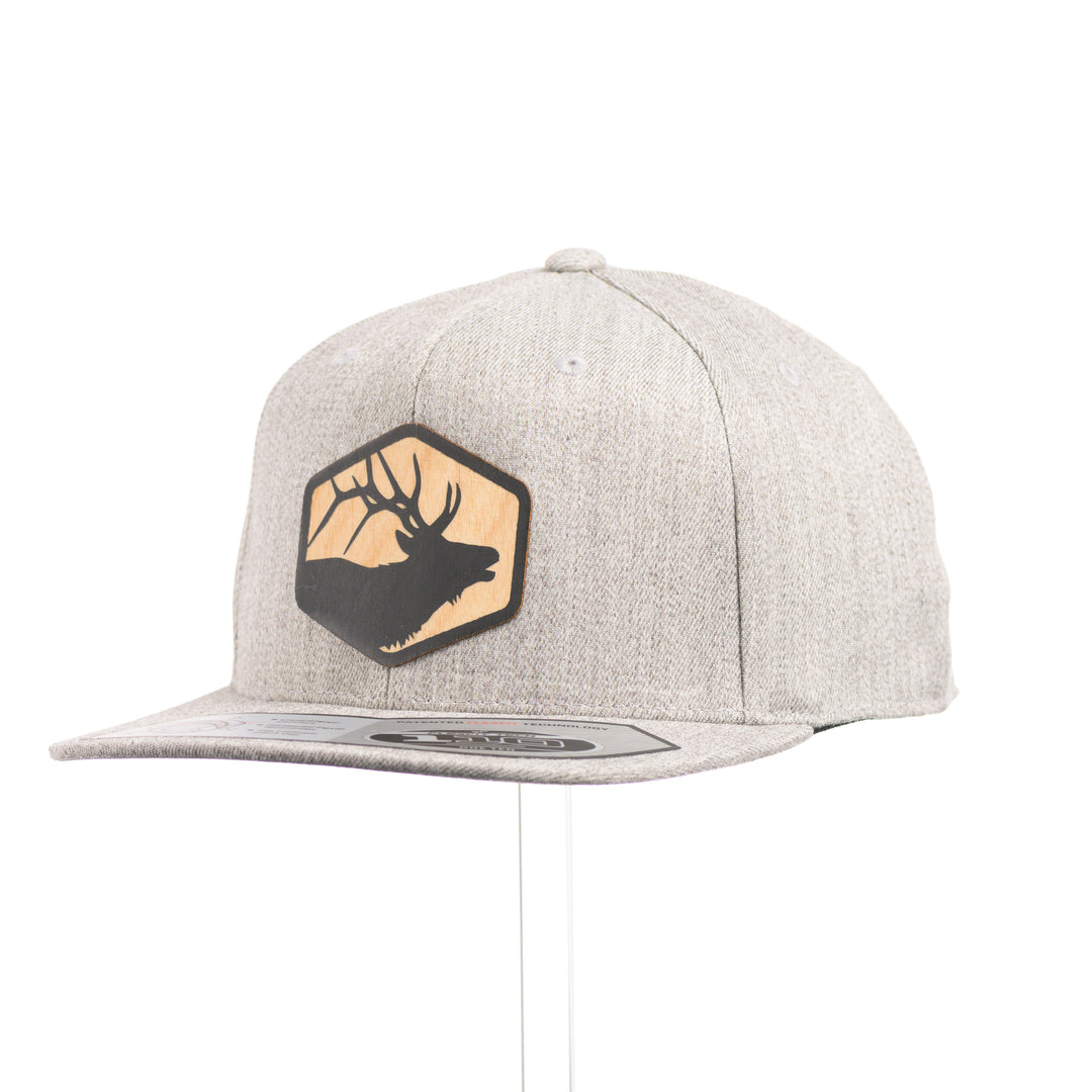 A heather grey flexfit flat bill hat with a hexagon elk silhouette flexwood patch at a quarter turn.