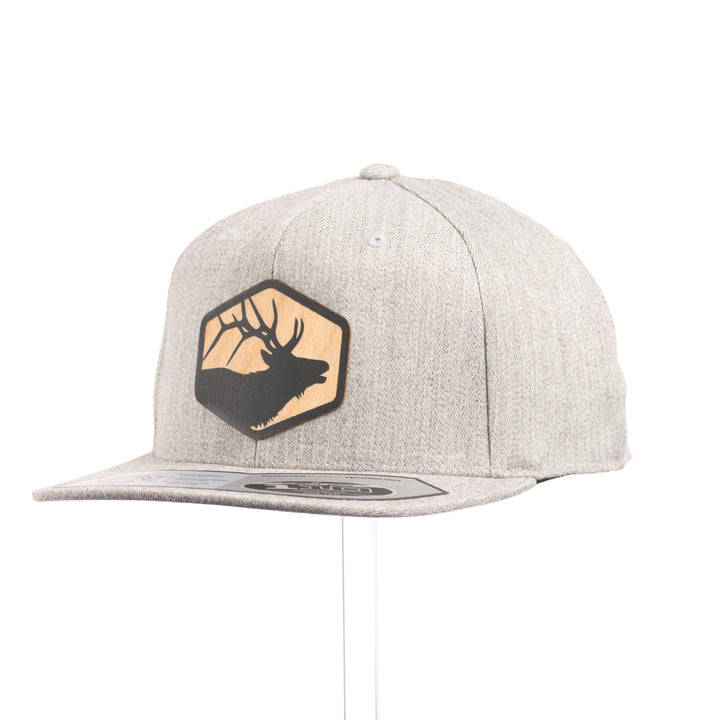 A heather grey flexfit flat bill hat with a hexagon elk silhouette flexwood patch at a quarter turn.