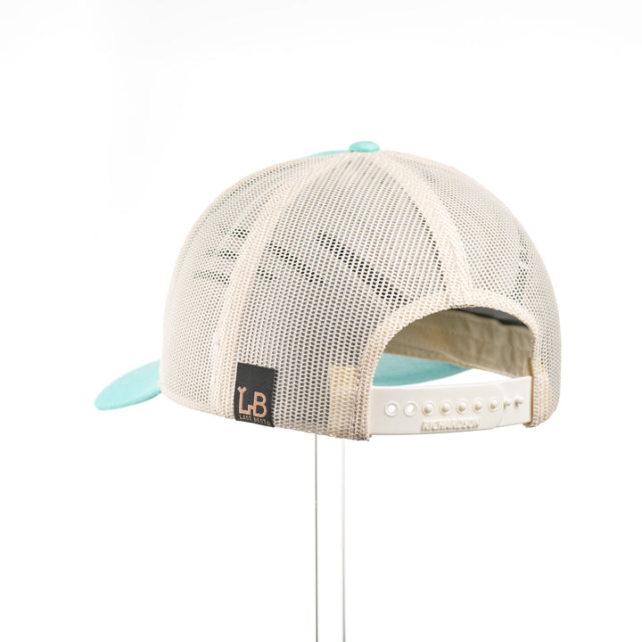 The back of a Cherry Wood Steer Skull w/ Paisley Teal & Cream Trucker Hat, featuring a hexagonal real cherry wood veneer patch with cut-out steer skull silhouette surrounded by etched paisley design, laminated to a hexagonal teal anodized aluminum plate, and riveted to a light teal and cream Richardson 115 low-profile trucker hat—handmade in Montana, USA by Last Best Supply Co.