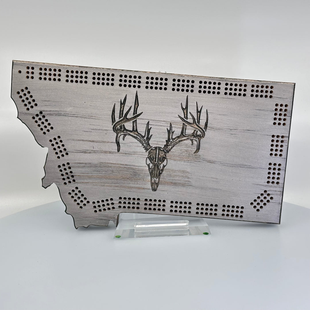 Knotty Pine Woodworks Handmade Montana Deer Skull Cribbage Board Grey (front)--this made in Montana wooden cribbage board is shaped like the outline of the state of Montana, painted grey,  and features an engraved deer skull on the front.