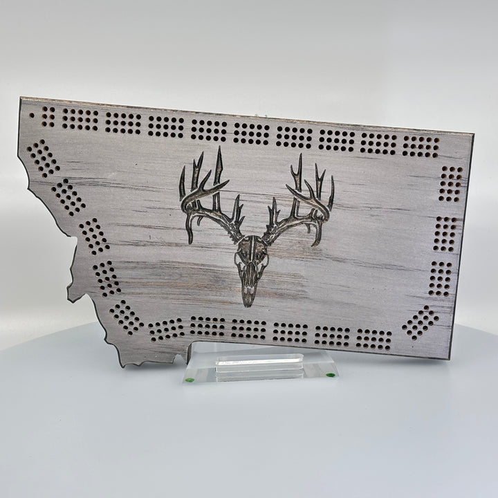 Knotty Pine Woodworks Handmade Montana Deer Skull Cribbage Board Grey (front)--this made in Montana wooden cribbage board is shaped like the outline of the state of Montana, painted grey,  and features an engraved deer skull on the front.