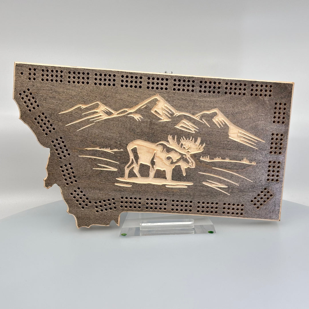 Knotty Pine Woodworks HandmadeMontana Moose Cribbage Board Ebony (front)--this made in Montana wooden cribbage board is shaped like the outline of the state of Montana, painted dark grey, and features an engraved moose standing in front of mountain peaks on the front.