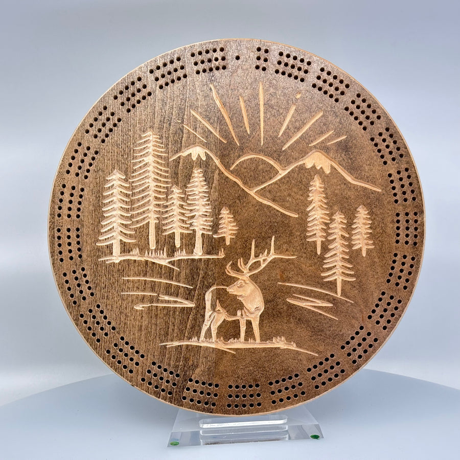 Knotty Pine Woodworks Handmade Mountain Elk Circle Cribbage Board Light Espresso (front)--this made in Montana wooden cribbage board is circular in shape with a light espresso finish, and features a beautifully engraved elk standing proudly against a backdrop of sunbeams framed by mountain peaks on the front.