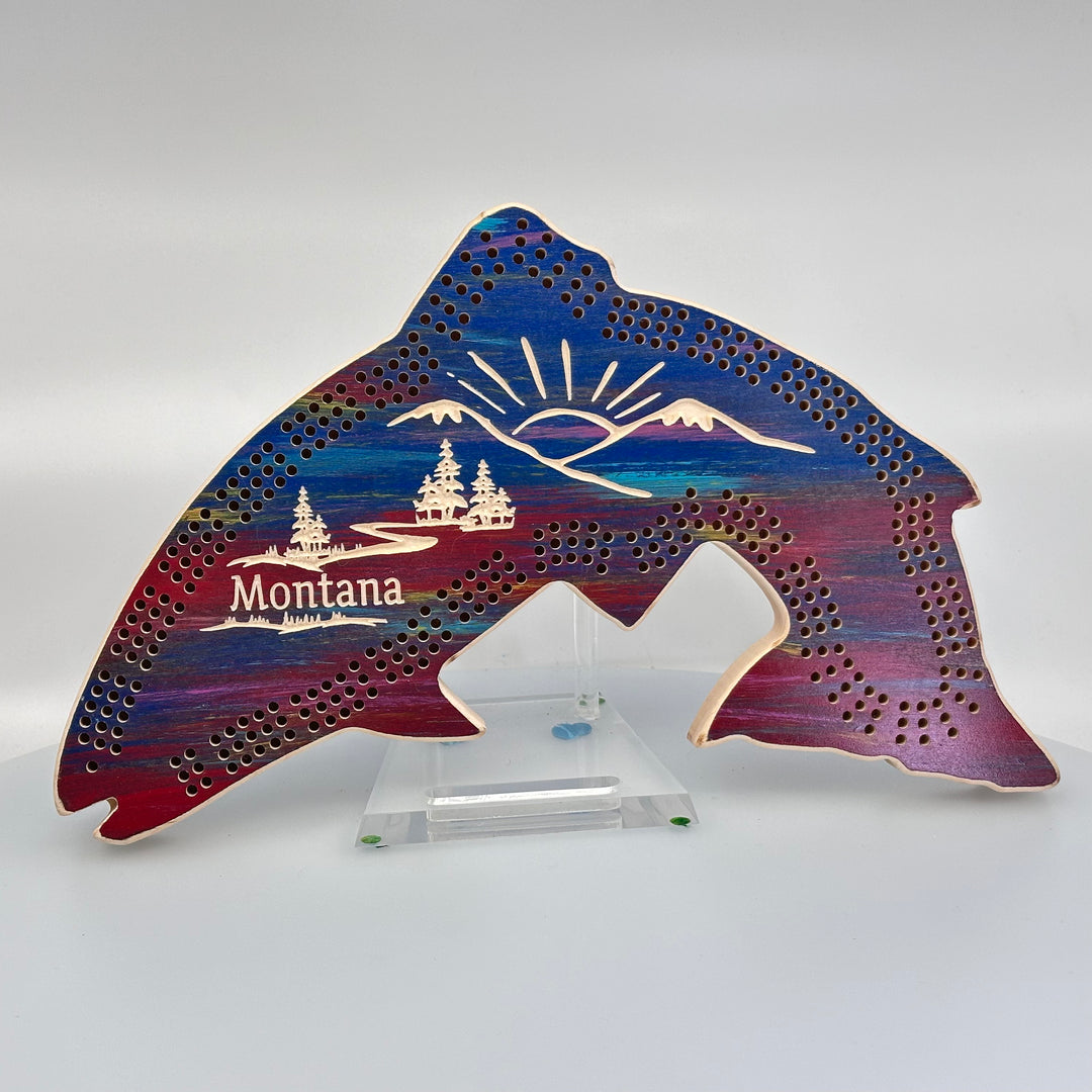 Knotty Pine Woodworks Handmade Trout Cribbage Board with Montana Mountain Scene Sunset (front)--this made in Montana wooden cribbage board is shaped like a leaping trout, finished in sunset tones, and features a beautifully engraved forest and mountain scene with the word ‘Montana’ engraved on the front.