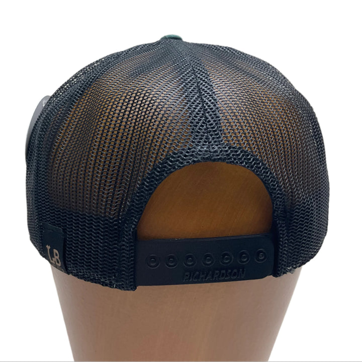 Back of a Bigfoot Face Flexwood Patch Forest Green Flat Bill Trucker Hat, featuring a circular Flexwood patch etched with a Bigfoot face design and securely attached to a forest green and black Richardson flat bill trucker hat—handmade in Montana, USA by Last Best Supply Co.