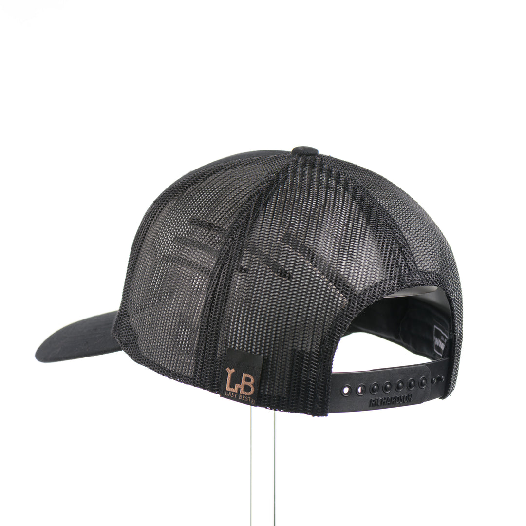 The back of an all black Richardson trucker hat with a black leather trout rectangle patch thick stitched on with black thread—handmade in Montana, USA by Last Best Supply Co.