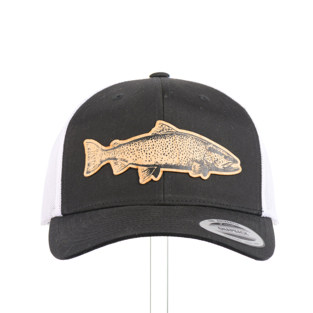 The front of a Sport-Tek Black & White Trucker Hat featuring a flexwood patch cut into the shape of a brown trout and etched with detail—handmade in Montana, USA by Last Best Supply Co.
