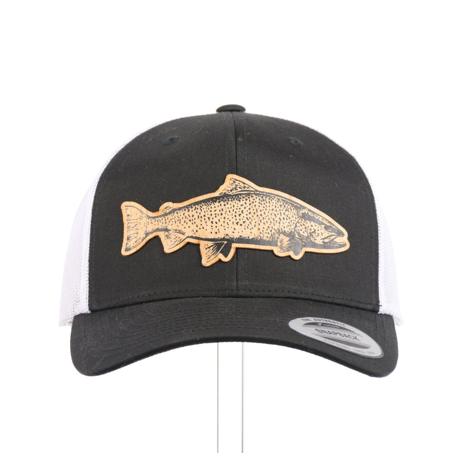 The front of a Sport-Tek Black & White Trucker Hat featuring a flexwood patch cut into the shape of a brown trout and etched with detail—handmade in Montana, USA by Last Best Supply Co.
