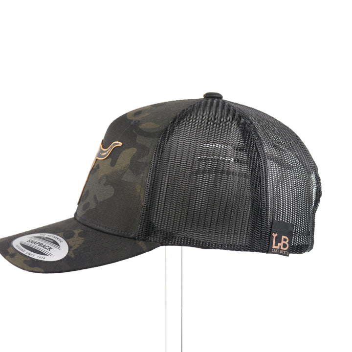 The side of a dark multicam trucker hat with a flexwood steer skull patch, handmade in Montana USA by Last Best Supply Co.