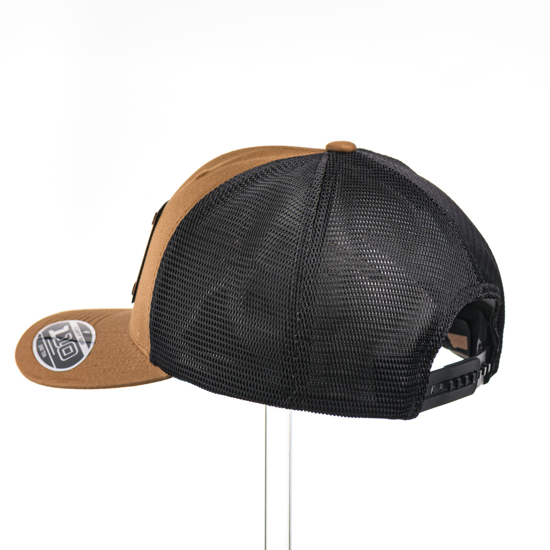 The back of a Cherry Wood & Red Copper Bison Coyote Brown & Black Trucker Hat, featuring a rectangular real cherry wood veneer patch with cut-out bison silhouette inlayed with red copper, laminated to a black anodized aluminum plate, and riveted to a coyote brown and black mesh Flexfit 110M trucker hat—handmade in Montana, USA by Last Best Supply Co.