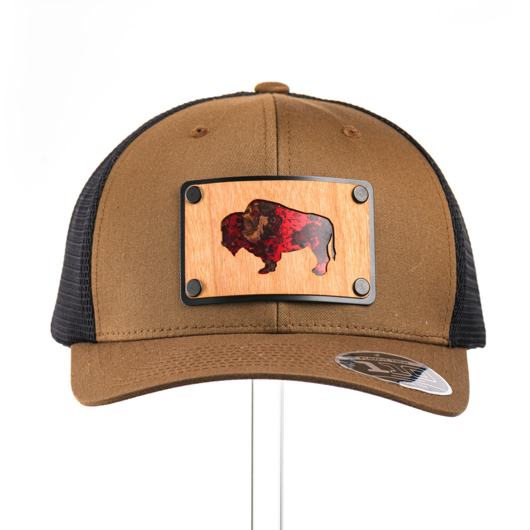 The front view of a Cherry Wood & Red Copper Bison Coyote Brown & Black Trucker Hat, featuring a rectangular real cherry wood veneer patch with cut-out bison silhouette inlayed with red copper, laminated to a black anodized aluminum plate, and riveted to a coyote brown and black mesh Flexfit 110M trucker hat—handmade in Montana, USA by Last Best Supply Co.