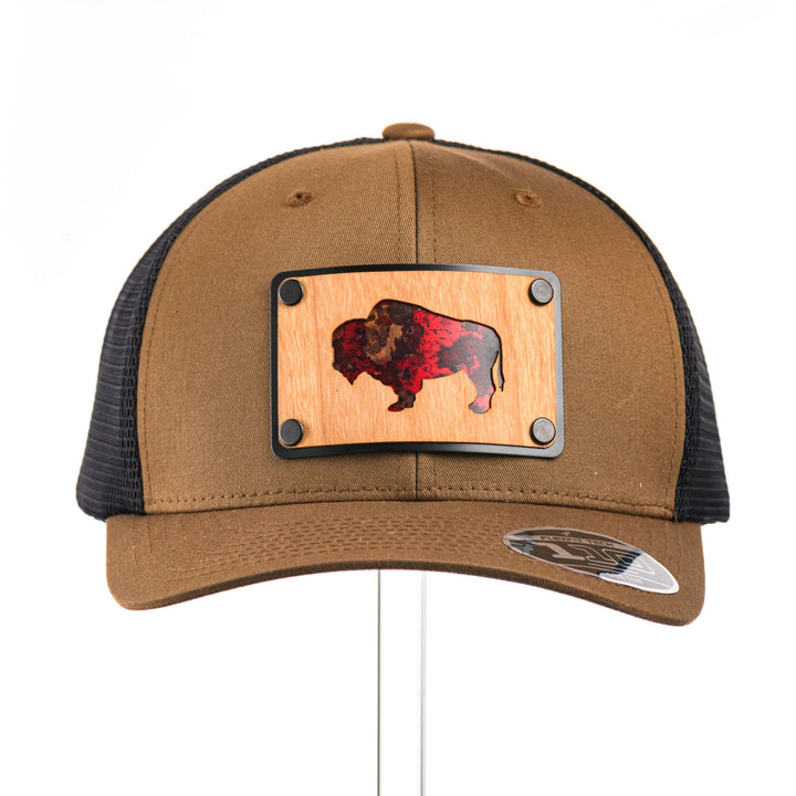 The front view of a Cherry Wood & Red Copper Bison Coyote Brown & Black Trucker Hat, featuring a rectangular real cherry wood veneer patch with cut-out bison silhouette inlayed with red copper, laminated to a black anodized aluminum plate, and riveted to a coyote brown and black mesh Flexfit 110M trucker hat—handmade in Montana, USA by Last Best Supply Co.