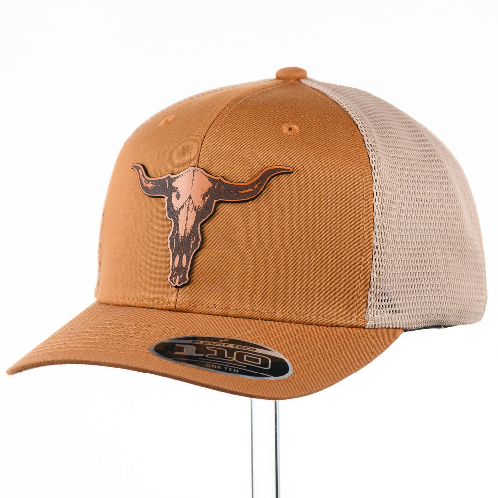 Etched Leather Bull Skull Patch Flexfit Trucker Hat, featuring a real leather patch cut into the shape of a steer skull and etched with detail, securely attached to a caramel and khaki trucker hat—handmade in Montana, USA by Last Best Supply Co.