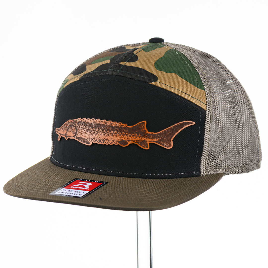 Etched Leather Sturgeon Patch on a Camo Tri-Colored Flat Bill Trucker Hat, featuring a real leather patch cut into the shape of a Sturgeon and etched with detail, securely attached to a Camo Tri-Colored flat bill trucker hat—handmade in Montana, USA by Last Best Supply Co.