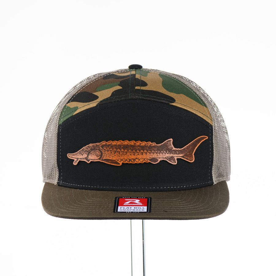 Etched Leather Sturgeon Patch on a Camo Tri-Colored Flat Bill Trucker Hat, featuring a real leather patch cut into the shape of a Sturgeon and etched with detail, securely attached to a Camo Tri-Colored flat bill trucker hat—handmade in Montana, USA by Last Best Supply Co.