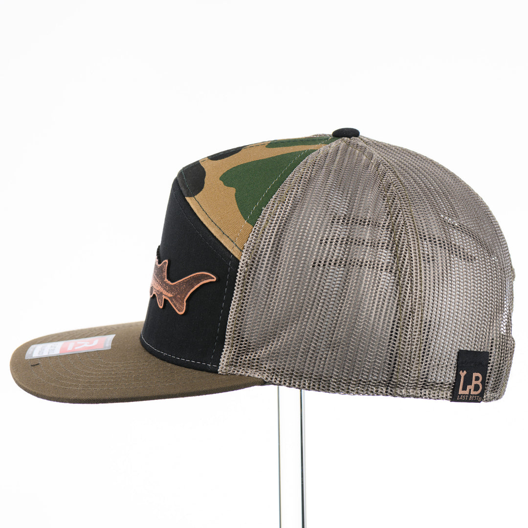 Etched Leather Sturgeon Patch on a Camo Tri-Colored Flat Bill Trucker Hat, featuring a real leather patch cut into the shape of a Sturgeon and etched with detail, securely attached to a Camo Tri-Colored flat bill trucker hat—handmade in Montana, USA by Last Best Supply Co.