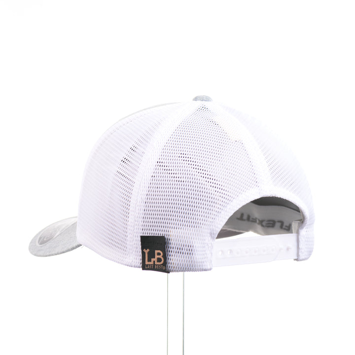 The back of a Mahogany Wood Jumping Trout Patch Flexfit Trucker Hat, featuring a real mahogany wood patch cut into the silhouette of trees, mounted on an anodized aluminum plate and secured with silver rivets to a heathered silver and white Flexfit trucker hat—handmade in Montana, USA by Last Best Supply Co.