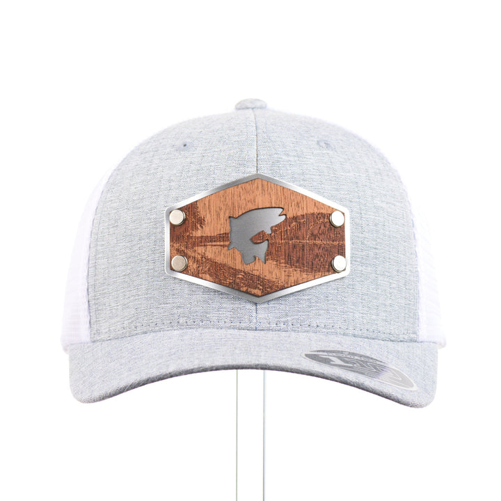 The front of a Mahogany Wood Jumping Trout Patch Flexfit Trucker Hat, featuring a real mahogany wood patch cut into the silhouette of trees, mounted on an anodized aluminum plate and secured with silver rivets to a heathered silver and white Flexfit trucker hat—handmade in Montana, USA by Last Best Supply Co.