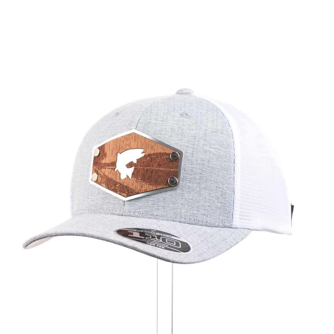 3/4 view of a Mahogany Wood Jumping Trout Patch Flexfit Trucker Hat, featuring a real mahogany wood patch cut into the silhouette of trees, mounted on an anodized aluminum plate and secured with silver rivets to a heathered silver and white Flexfit trucker hat—handmade in Montana, USA by Last Best Supply Co.