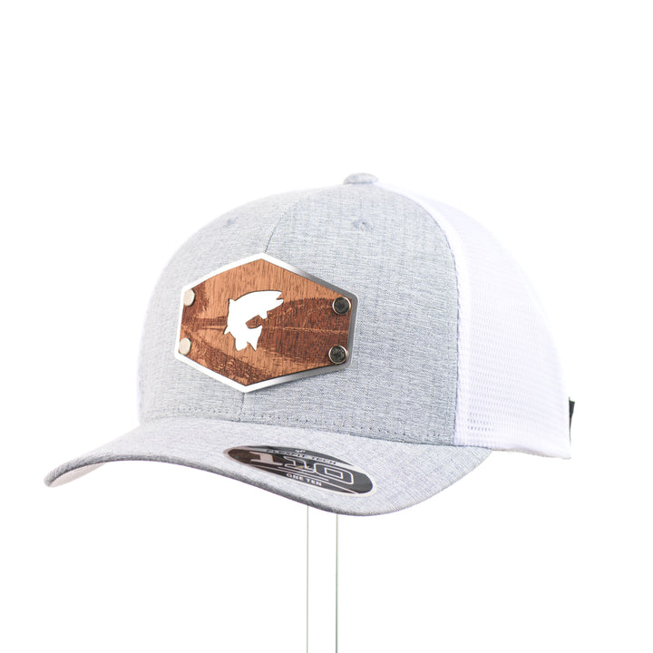 3/4 view of a Mahogany Wood Jumping Trout Patch Flexfit Trucker Hat, featuring a real mahogany wood patch cut into the silhouette of trees, mounted on an anodized aluminum plate and secured with silver rivets to a heathered silver and white Flexfit trucker hat—handmade in Montana, USA by Last Best Supply Co.