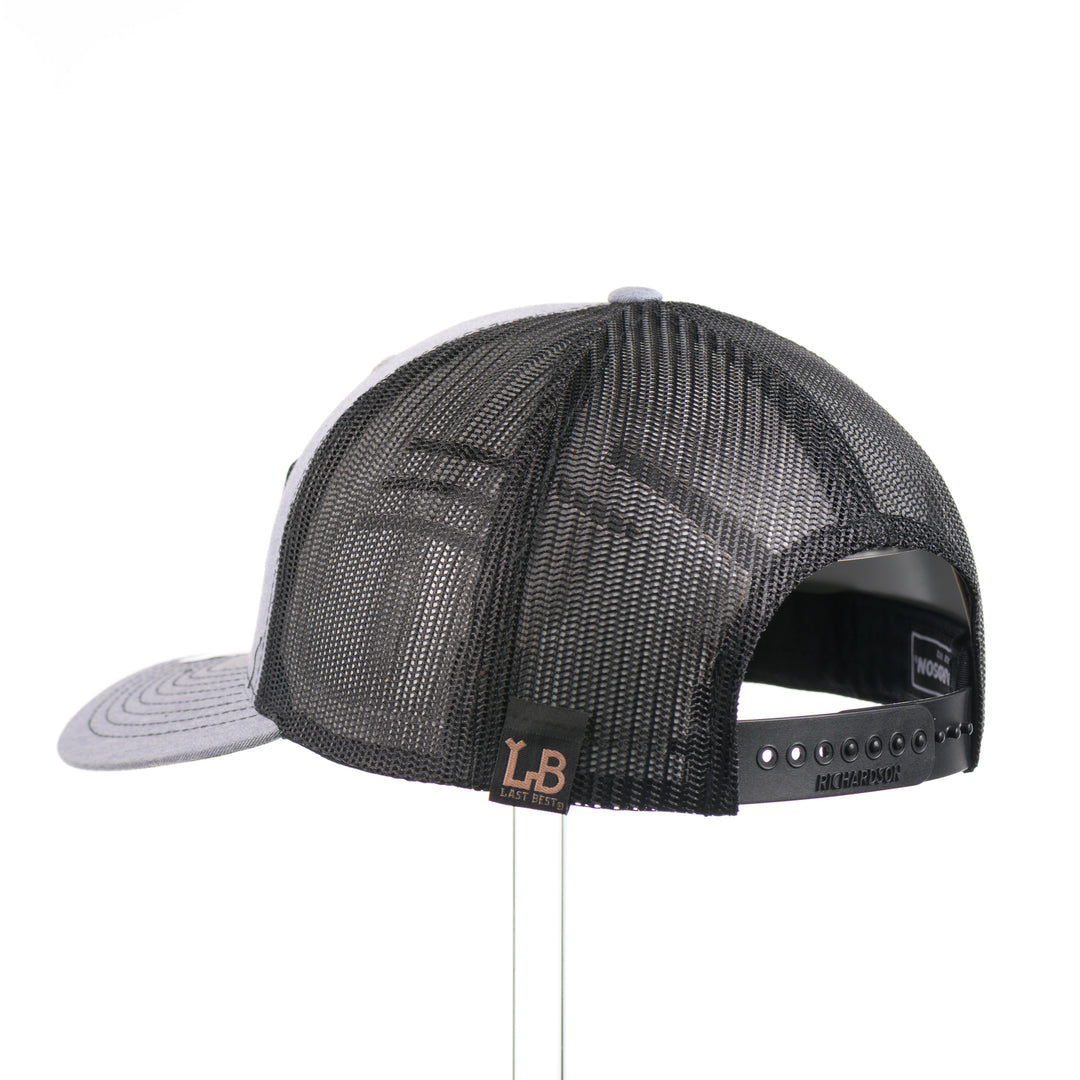 The back of a heather gray and black Richardson trucker hat with an etched walnut wood American flag and elk patch on a hexagon metal plate, handmade in Montana, USA by Last Best Supply Co.