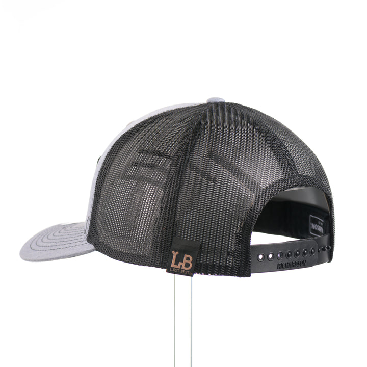 The back of a heather gray and black Richardson trucker hat with an etched walnut wood American flag and elk patch on a hexagon metal plate, handmade in Montana, USA by Last Best Supply Co.