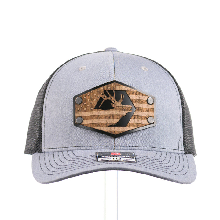 The front of a heather gray and black Richardson trucker hat with an etched walnut wood American flag and elk patch on a hexagon metal plate, handmade in Montana, USA by Last Best Supply Co.
