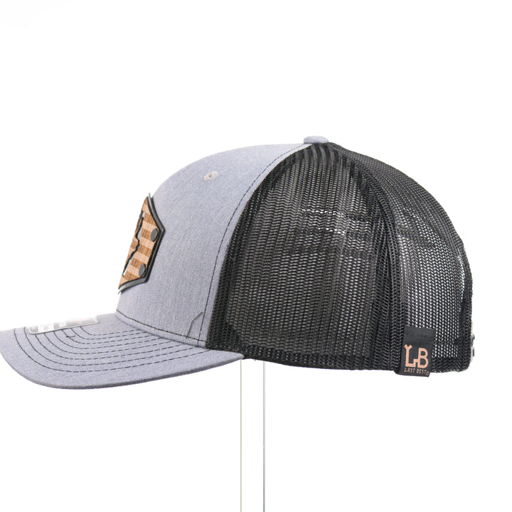 The side of a heather gray and black Richardson trucker hat with an etched walnut wood American flag and elk patch on a hexagon metal plate, handmade in Montana USA by Last Best Supply Co.