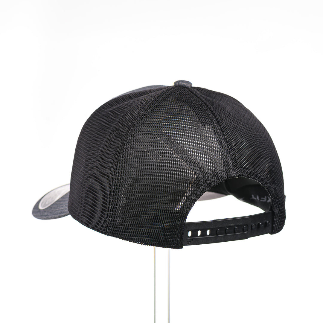 The back of a Mahogany Wood Elk Patch Flexfit Trucker Hat, featuring a real mahogany wood veneer patch precision-cut into a hexagon shape with a bold elk silhouette cut-out, laminated to a matching anodized aluminum plate, and riveted to a charcoal and black Flexfit 110F flat bill hat—handmade in Montana, USA by Last Best Supply Co.