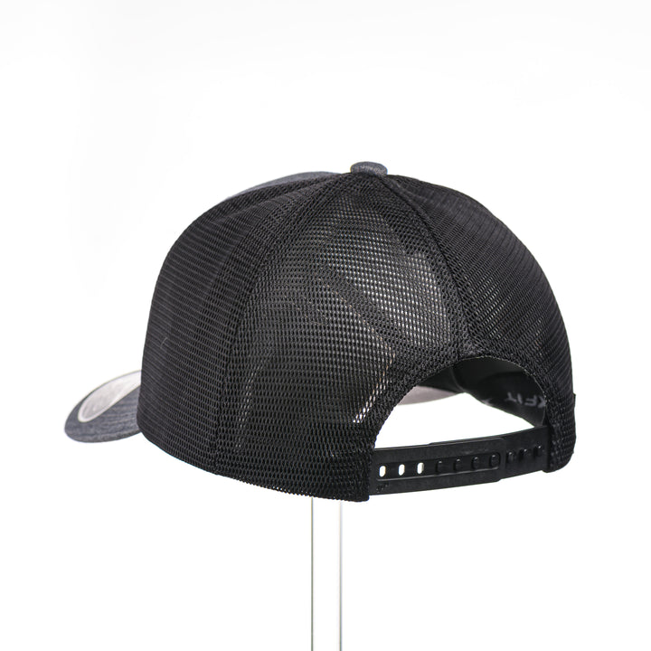 The back of a Mahogany Wood Elk Patch Flexfit Trucker Hat, featuring a real mahogany wood veneer patch precision-cut into a hexagon shape with a bold elk silhouette cut-out, laminated to a matching anodized aluminum plate, and riveted to a charcoal and black Flexfit 110F flat bill hat—handmade in Montana, USA by Last Best Supply Co.