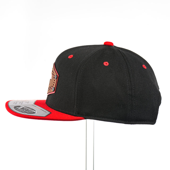 The side of a Grizzly Bear w/ Lines Walnut Wood Black & Red Flat Bill Hat, featuring a hexagonal real walnut wood veneer patch with a cut-out bear silhouette and fine line details, laminated to a hexagonal red anodized aluminum plate, and riveted to a black and red Flexfit 110F flat bill hat—handmade in Montana, USA by Last Best Supply Co.