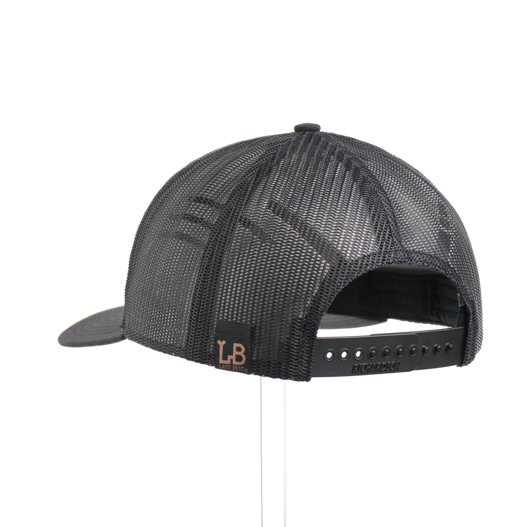 The back of a Mahogany Wood Tines American Flag Patch Trucker Hat, featuring a real walnut wood veneer patch etched with an American flag and cut-out elk antler tines, laminated to a black anodized aluminum plate and riveted to an all-black Richardson 112 trucker hat along—handmade in Montana, USA by Last Best Supply Co.