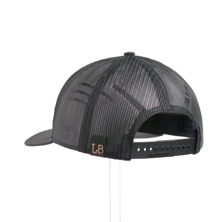 The back of a Mahogany Wood Tines American Flag Patch Trucker Hat, featuring a real walnut wood veneer patch etched with an American flag and cut-out elk antler tines, laminated to a black anodized aluminum plate and riveted to an all-black Richardson 112 trucker hat along—handmade in Montana, USA by Last Best Supply Co.