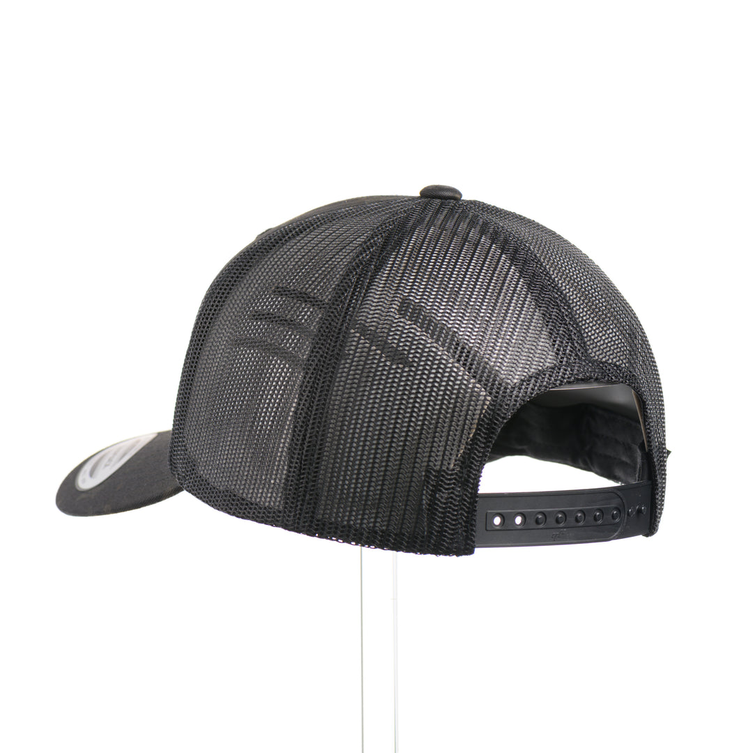 The back of a Snowy Bigfoot Leather Patch Black Camo Trucker Hat, featuring a circular real hand-dyed leather patch etched with a detailed Bigfoot in ski googles design, securely heat bonded and sewn onto the structured front of a dark camo Yupoong Retro Trucker Hat—handmade in Montana, USA by Last Best Supply Co.