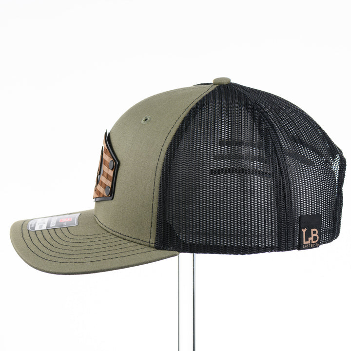 Walnut Wood Bigfoot American Flag Patch Trucker Hat featuring a real walnut wood patch laminated to a hexagon-shaped black anodized aluminum plate with an etched American flag and Bigfoot design, handmade in Montana, USA by Last Best Supply Co.