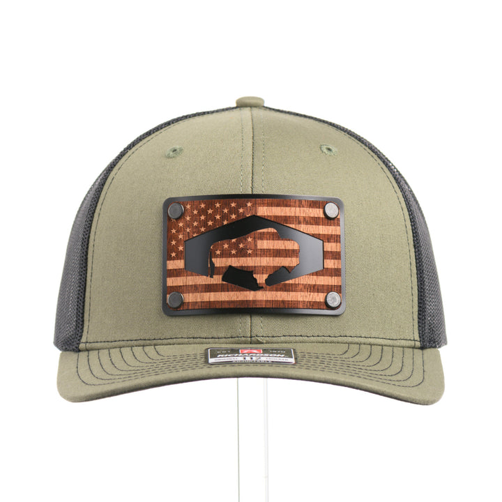 The front of a loden green and black mesh Richardson trucker hat with an etched walnut wood American flag and bison cut out on a black metal patch—handmade in Montana, USA by Last Best Supply Co.