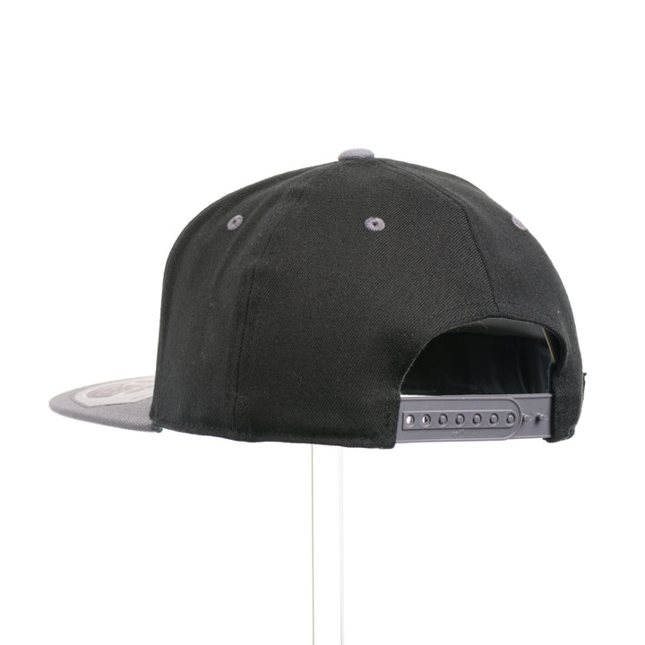 The back of a Walnut Wood Tines Flexfit Black & Grey Flat Bill Hat, featuring a real walnut wood veneer patch precision-cut into a hexagon with bold cut-out elk antler tines, laminated to a hexagon silver anodized aluminum plate, and riveted to a heather gray and black Flexfit 110F trucker hat—handmade in Montana, USA by Last Best Supply Co.