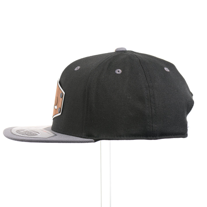 The side of a Walnut Wood Tines Flexfit Black & Grey Flat Bill Hat, featuring a real walnut wood veneer patch precision-cut into a hexagon with bold cut-out elk antler tines, laminated to a hexagon silver anodized aluminum plate, and riveted to a heather gray and black Flexfit 110F trucker hat—handmade in Montana, USA by Last Best Supply Co.