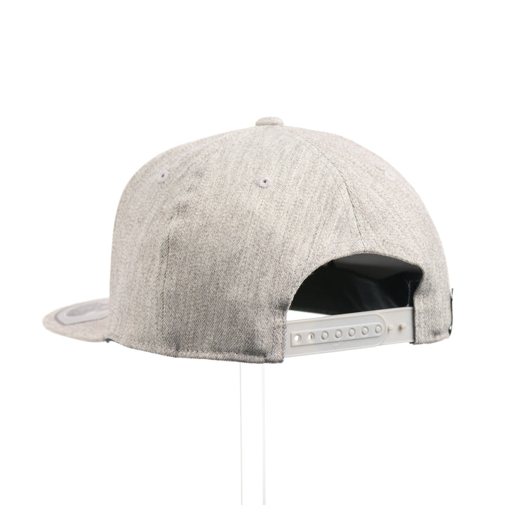 The back of a Walnut Trout Patch Plate Heather Grey Flat Bill Hat, featuring a rectangular real walnut wood veneer patch with cut-out trout silhouette, laminated to a black anodized metal plate, and riveted to a light heather grey 6-panel Flexfit Flat Bill Hat—handmade in Montana, USA by Last Best Supply Co.