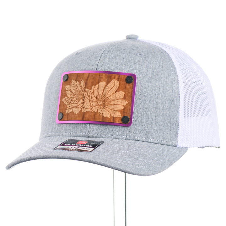 Gray and white cap with a wood and metal patch featuring a Bitterroot flower design on a white background